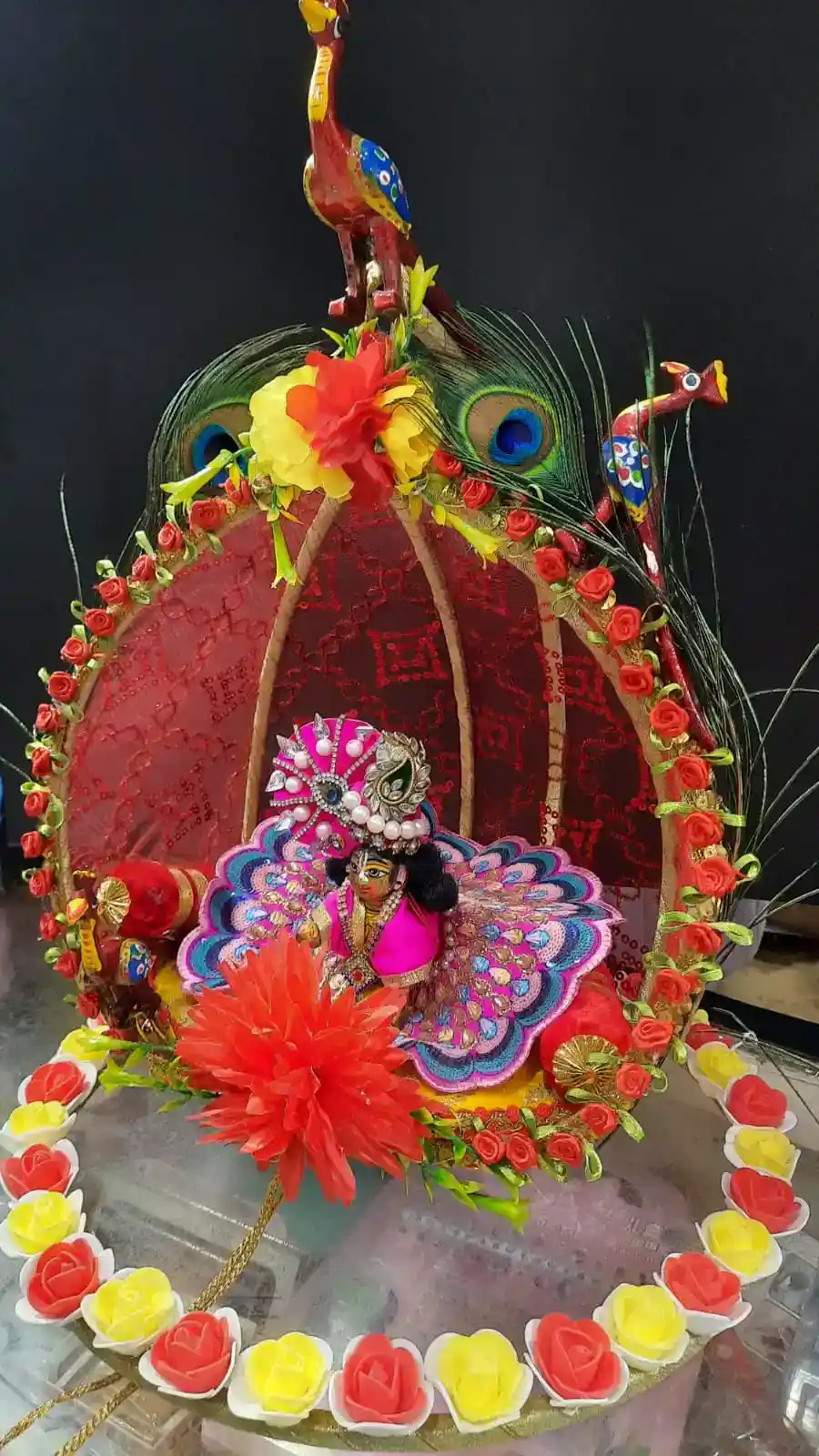 Devotional Laddu Gopal idol in an ornate peacock chariot adorned with colorful floral shringaar